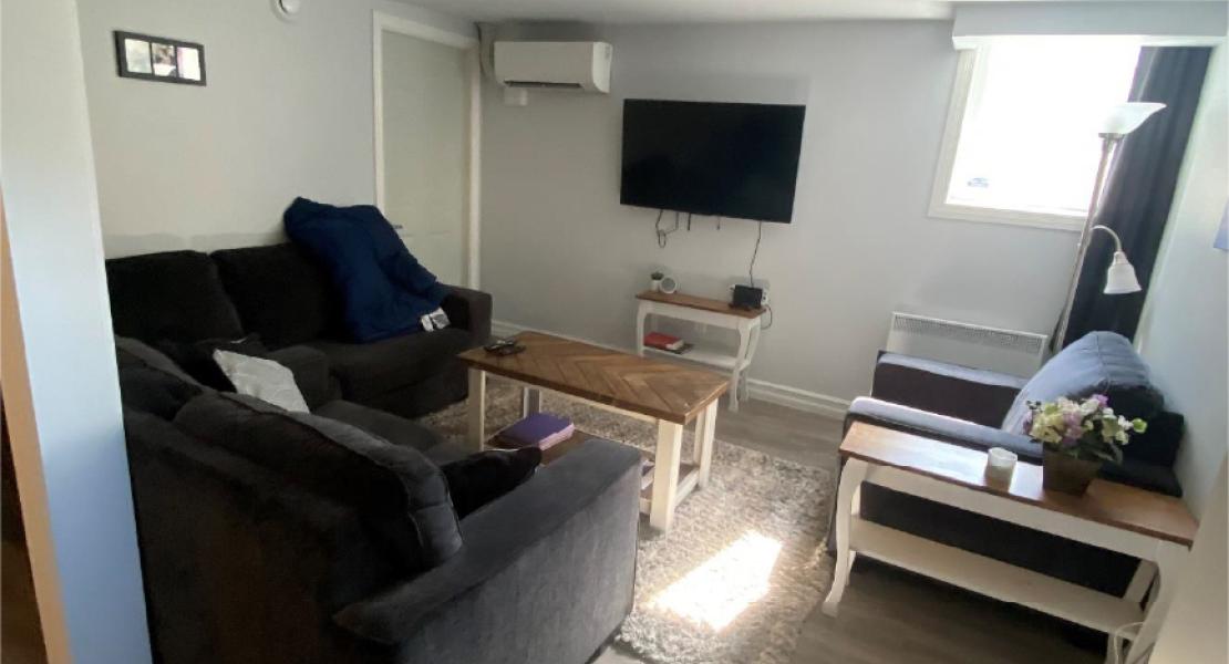 Living room with wood flooring, a TV, two couches, a chair, coffee table and rug 