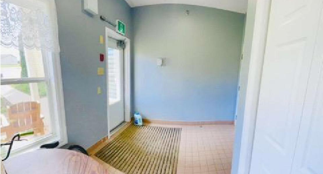 Bright hallway with light blue walls, exit door, window with lace curtain and floor mat. 