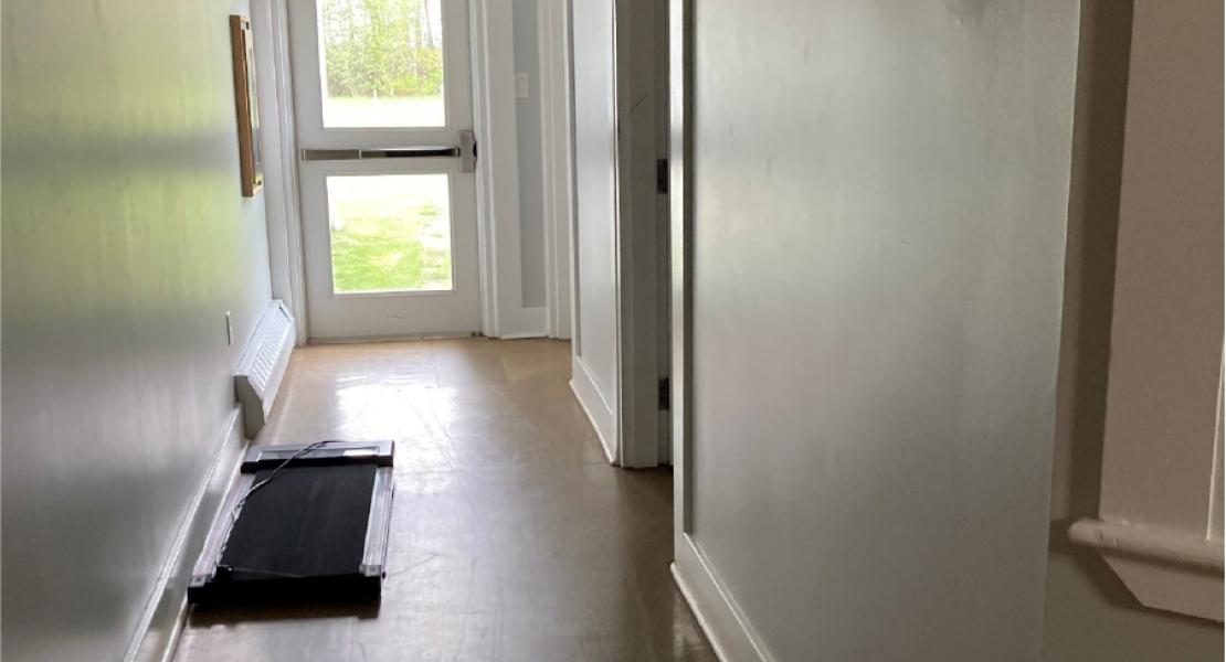 Long hallway with exit door at the end. Walking pad on the floor in the middle of the hallway. Another door to the right of the hallway. 