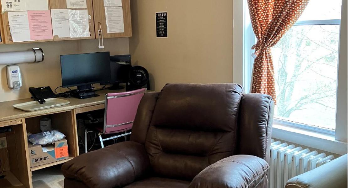 Desk with computer and a brown chair in front of a window with a polka dot curtain 