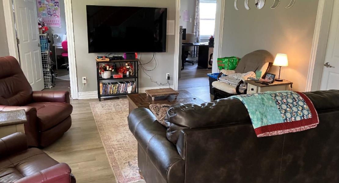 living room with a TV, a couch, two reclining chairs and two doorways leading off the living room to an office and bedroom.