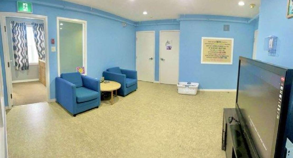 Blue walled room with two blue chairs, small table, double doors, TV screen and three visible doorways