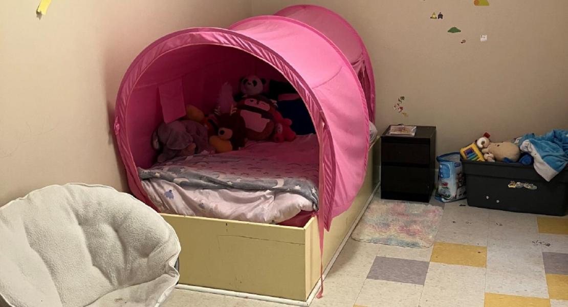 Children’s room with pink tent bed, wall decals, toys, checkered floor tiles and a white saucer chair 