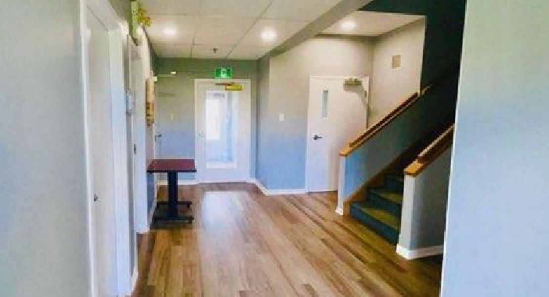 Hallway with wood flooring, staircase to the right, exit door ahead, and small table near the left wall. 