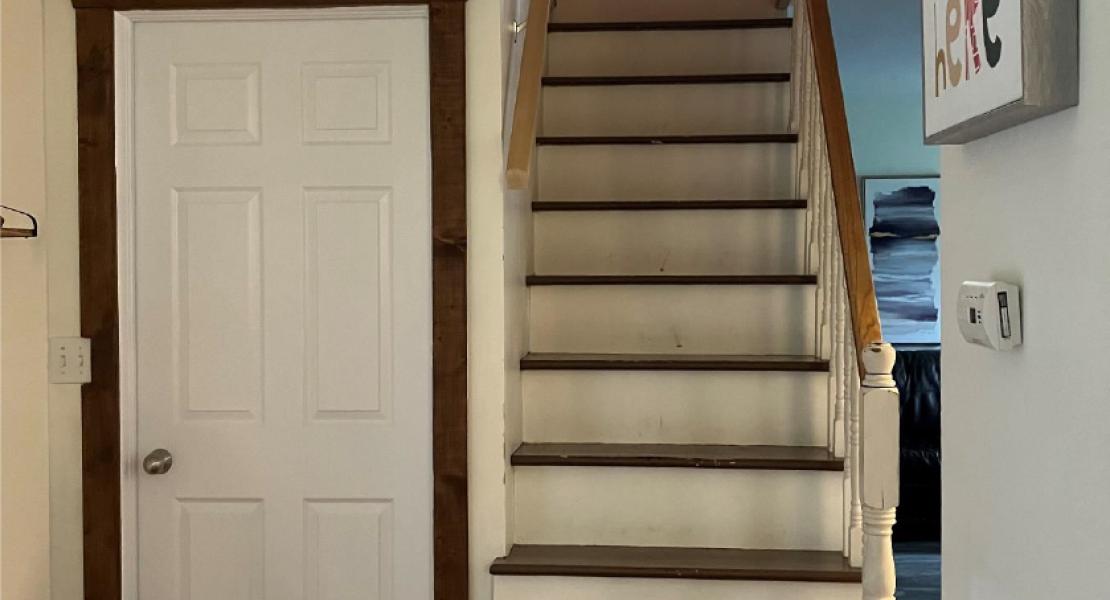  Hallway area with wooden floors and a door to the left of a wooden staircase leading to a second floor