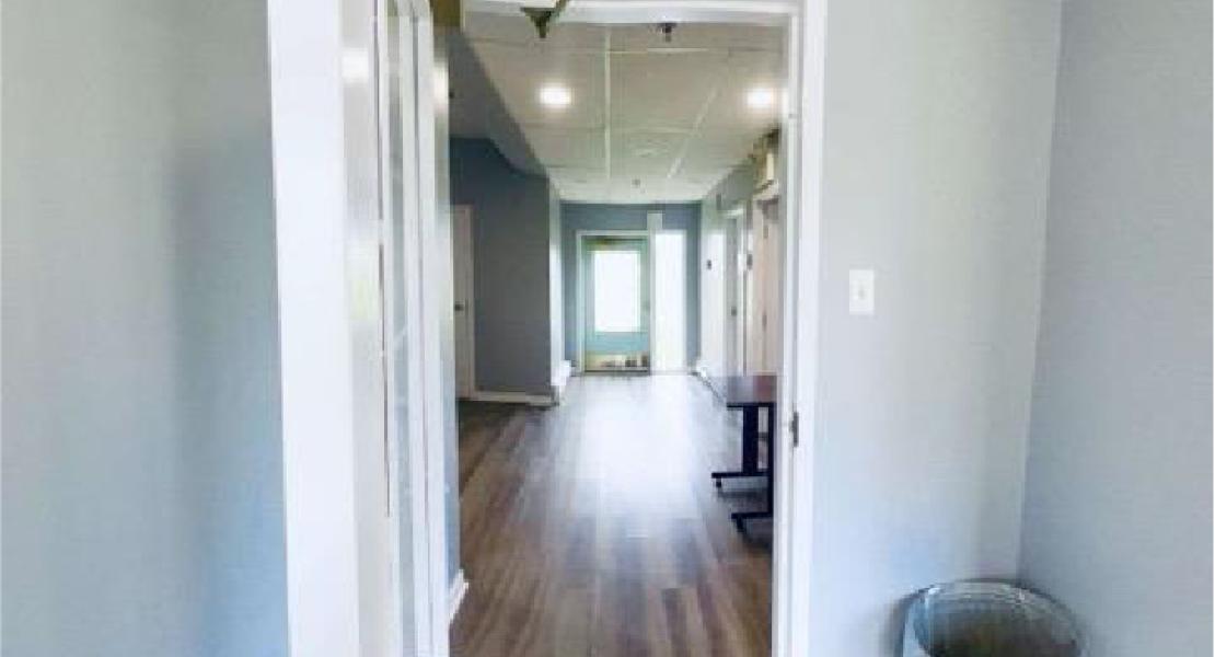 Open door heading to hallway with wood floors, blue walls, a trash bin, a door, and a small desk in the distance