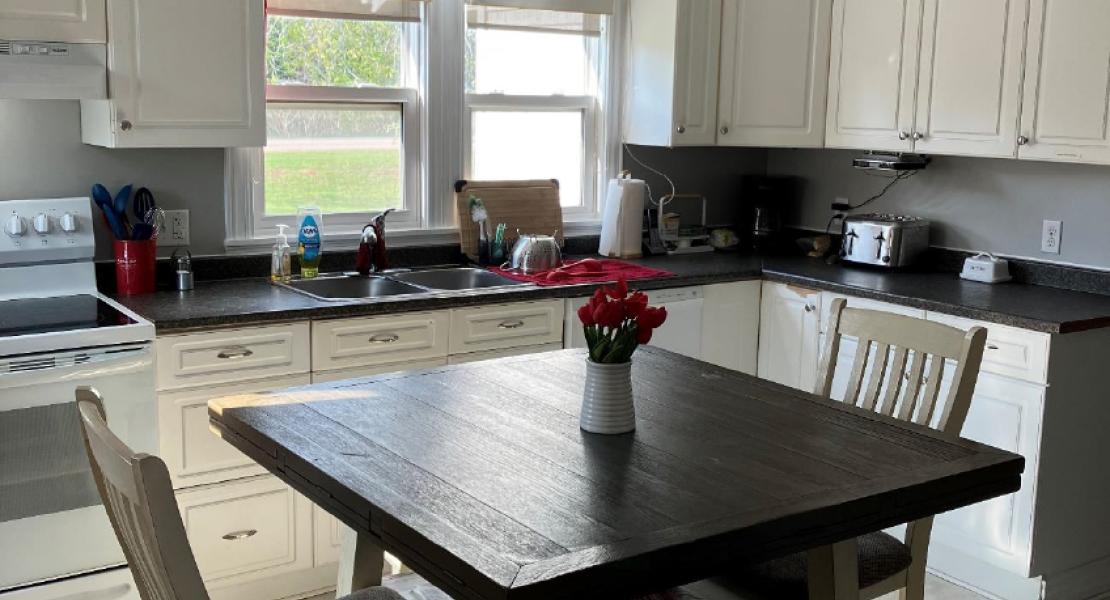 A kitchen with a table and chairs, a stove, and double sink under a bright window 