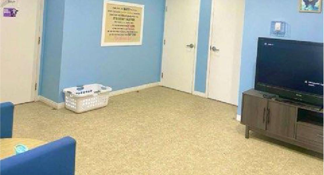 Room with blue walls, TV on stand, two blue chairs, basket on floor, and three closed white doors 