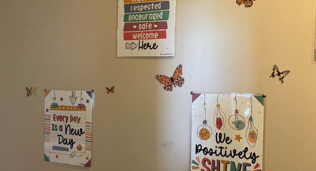A beige wall with three colorful, motivational posters and butterfly decals 