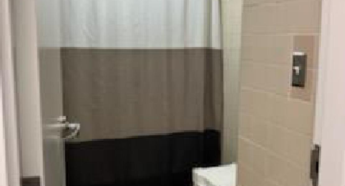 Bathroom view from the doorway. White, brown and black shower curtain covering a bathtub. Tiled floor with light bathmat.