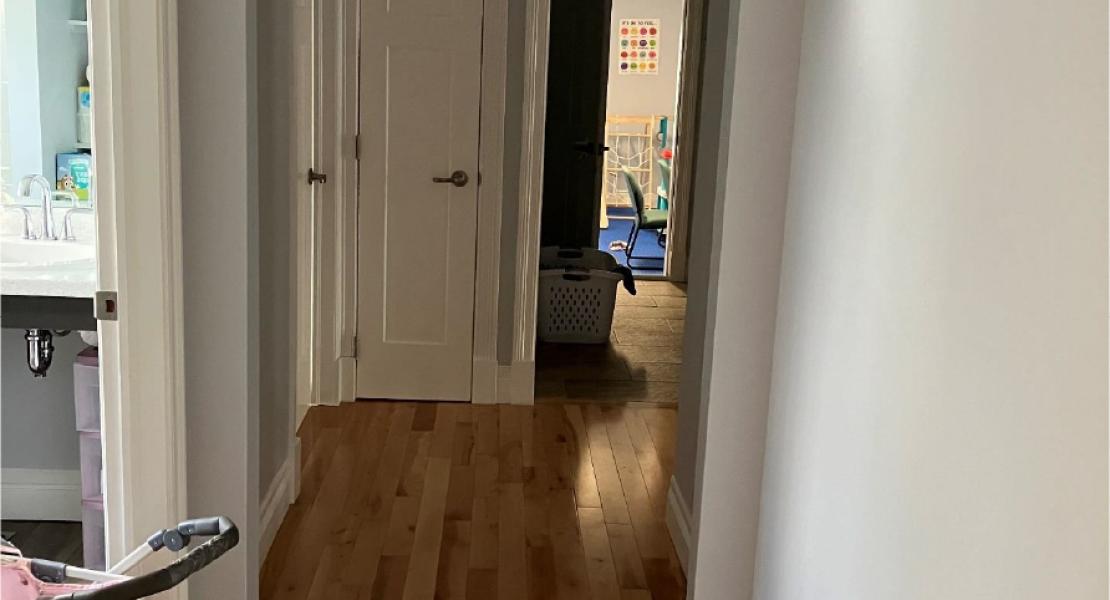 Hallway with wood flooring, closed closet door. Bathroom to the left and a children’s sensory room visible at the far end 