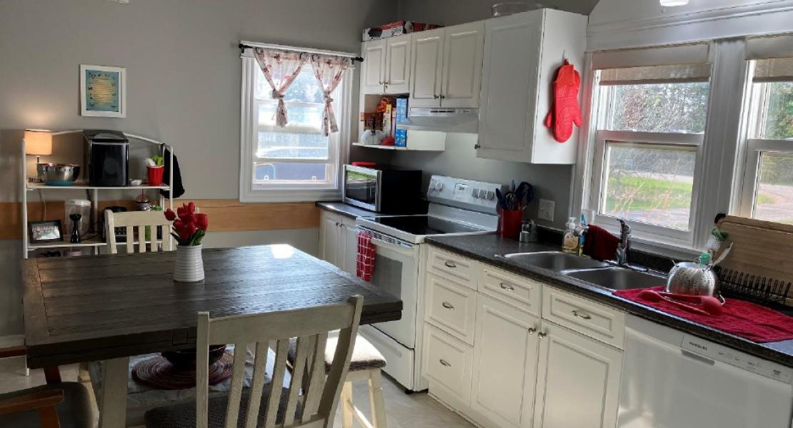 Kitchen with a table and chairs, a microwave, stove, double sink and three bright windows 