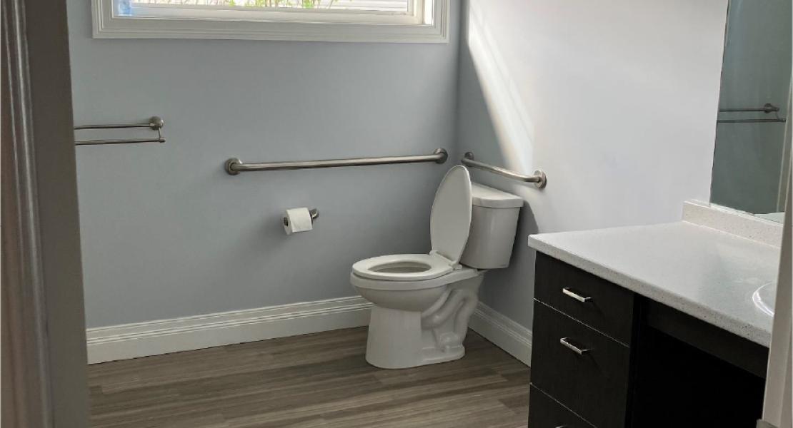 Accessible bathroom with grab bars, a toilet, large countertop with drawers, and wood style flooring 