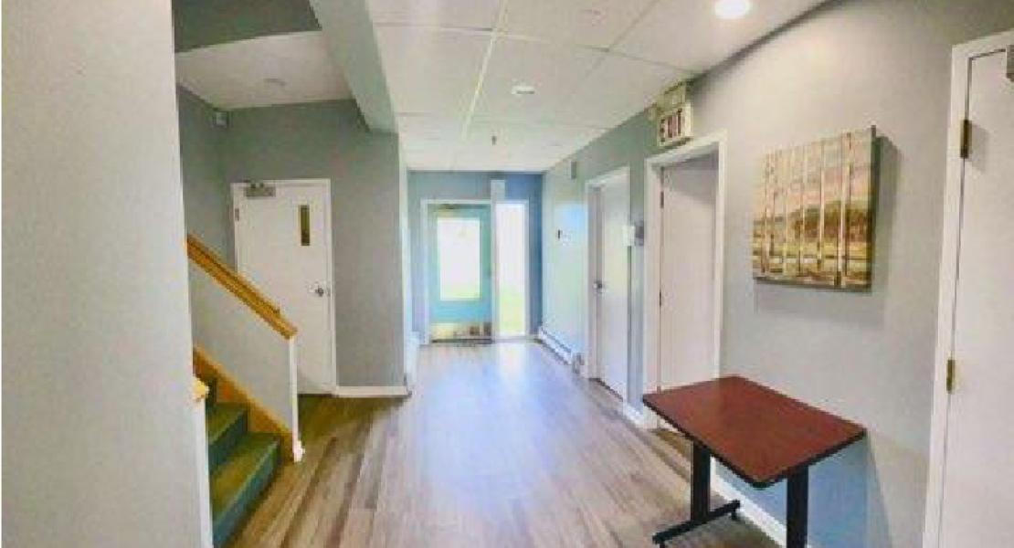 Bright hallway with wooden flooring, white doors, and a staircase on the left 