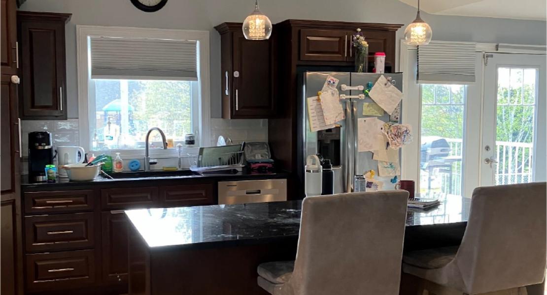 Kitchen with dark cabinets, large island with barstools, hanging pendant lights, stainless steel fridge and bright windows 