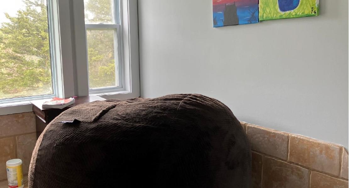 A tiled corner room with a large, bright window, colouring paintings on the wall and a large beanbag chair 