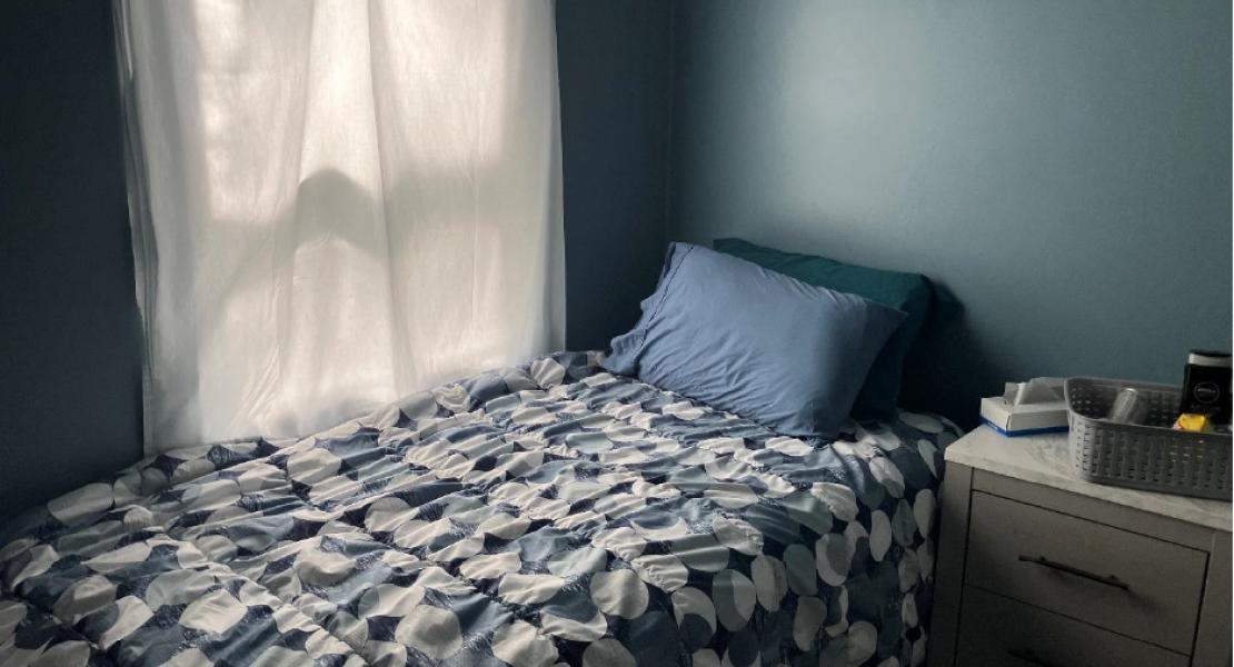 Cozy bedroom with single bed, blue bedding, and a white nightstand near a window 