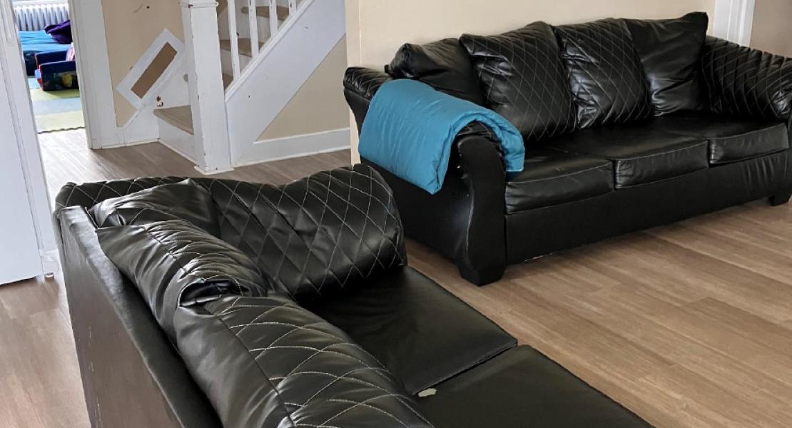 Living room with two black leather couches, a blue blanket, wood flooring, and a white staircase in the background