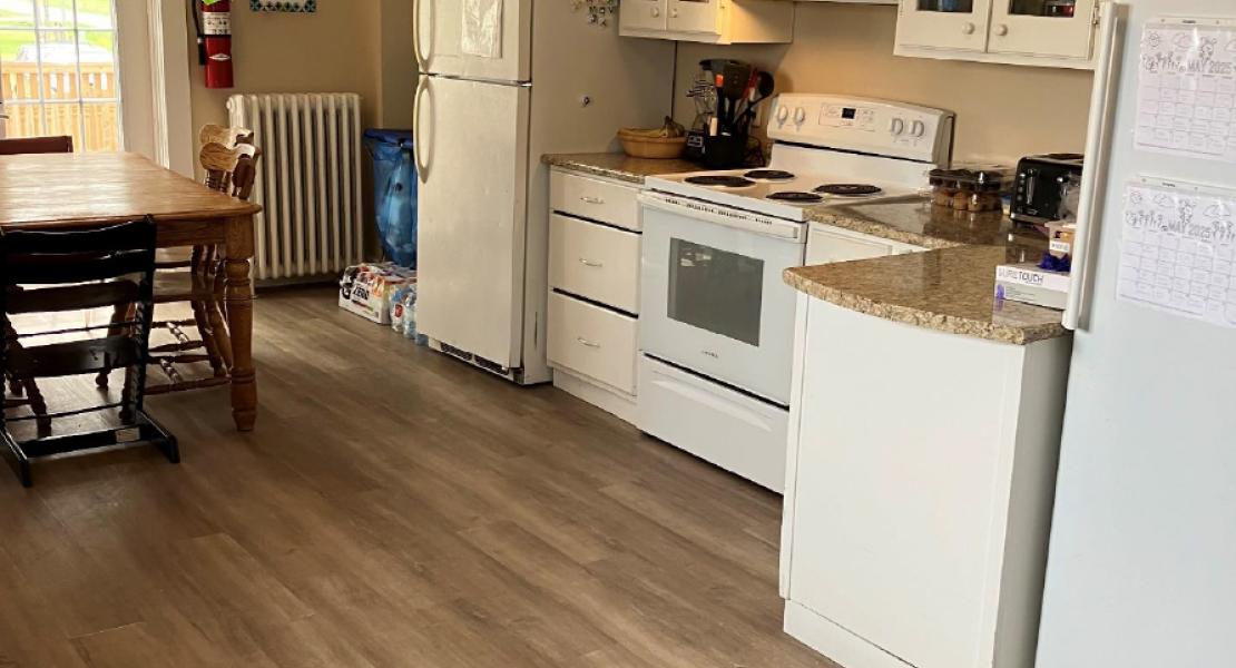 Spacious kitchen with white cabinets, wood flooring, dining table, and appliances including fridge, stove and dishwasher 