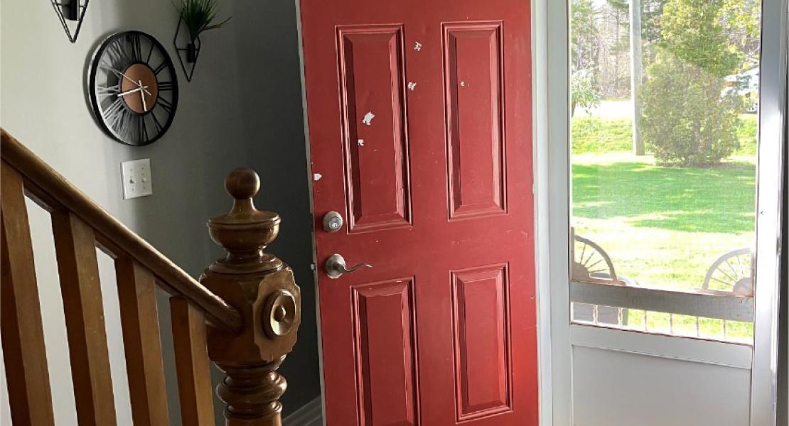 Bright entryway with open red door, checkered rug and screen door that leads to an oak wood staircase going up to the second floor. 
