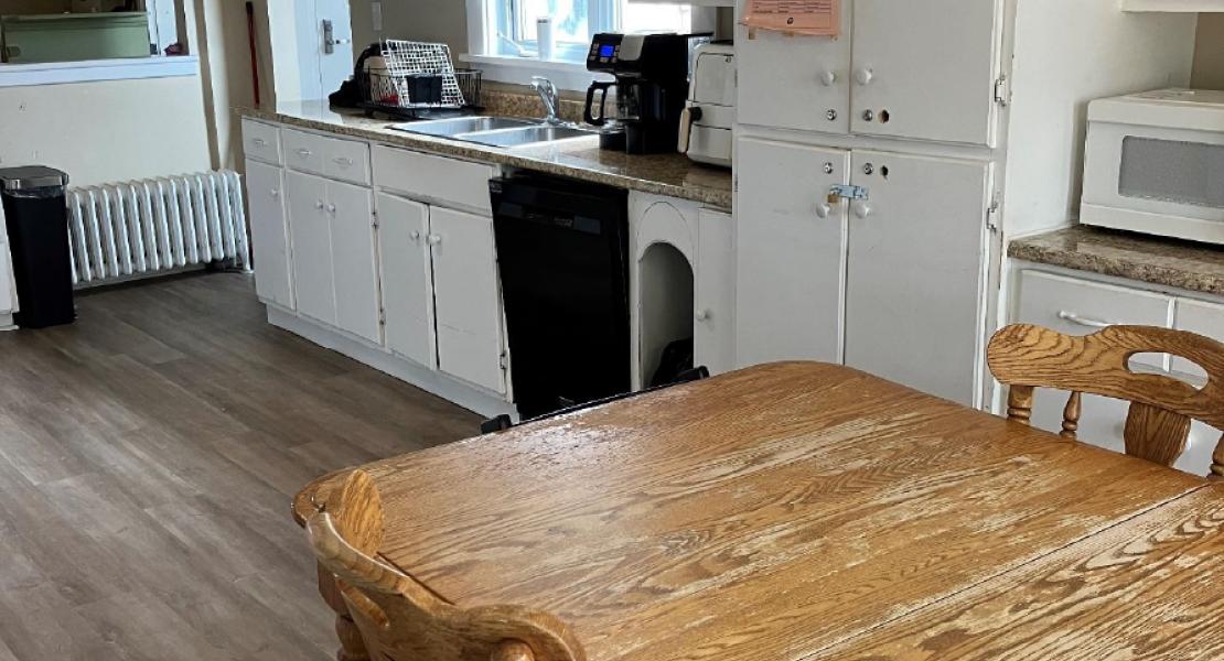  Kitchen with wood floors, white cabinets, large window, and a wooden dining table with backing chairs in the foreground 
