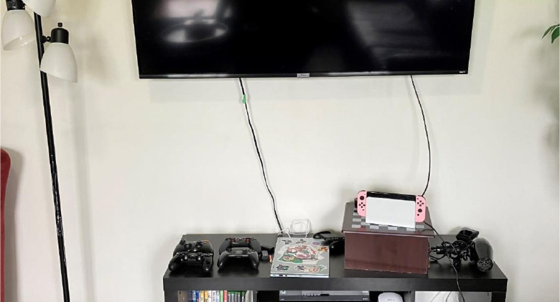 Livingroom wall with wood-like floors, a floor lamp, an entertainment center with gaming equipment and games under a mounted tv. 