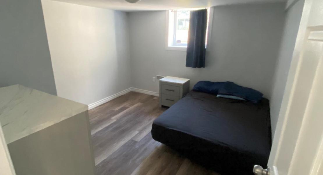 Bedroom with wood floors, dresser, nightstand and bed with dark sheets 
