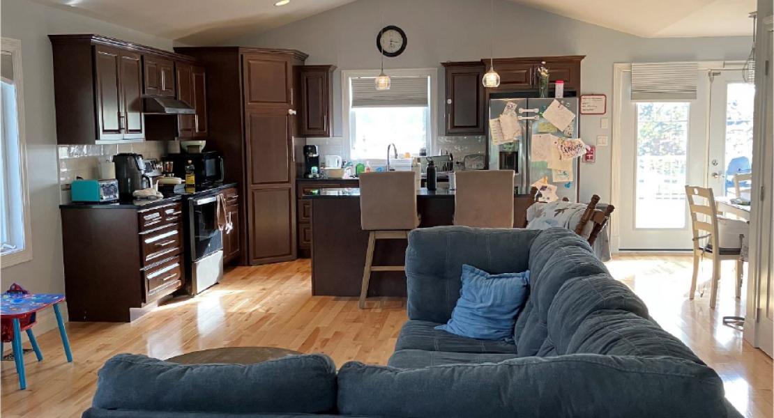 Open-concept living area with dark sectional couch, wood floors, and a kitchen with dark cabinets and island seating 