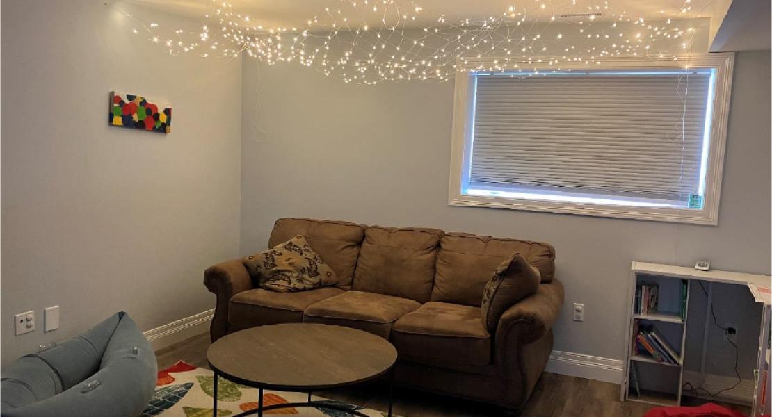 Cozy room with a brown couch, round coffee table, colourful rug, fairy lights on the ceiling, bean bag chair, and a small desk. 