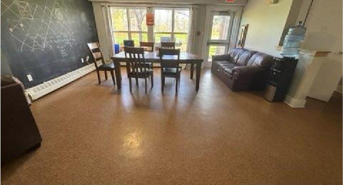 Dining room with chalkboard wall, table and chairs and a brown couch next to a water dispenser 